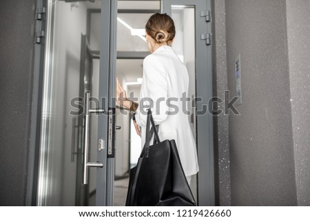 Young business woman in white suit entering to the hall of the modern residential building, back view Royalty-Free Stock Photo #1219426660