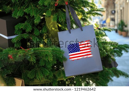 United States flag printed on a Christmas shopping bag. Close up of a shopping bag as a decoration on a Xmas tree on a street in America. Christmas shopping in USA, sale and deals concept. 