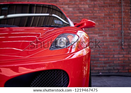 Close up of headlight detail of modern luxury sportscar with reflection on red paint after wash & wax. Front view of supercar with brick wall. Concept of car detailing and paint protection background. Royalty-Free Stock Photo #1219467475