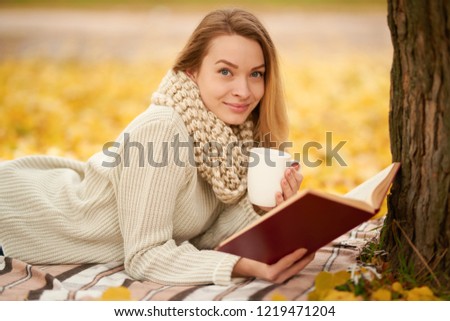 A beautiful girl reads a book and drinks warm tea, hot shikolad, coffee in a warm autumn park. Concept of autumn warmth, atmosphere and comfort. With space for an inscription