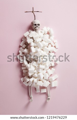 a skeleton covered with white sugar cubes like a tomb with a cross on a pink background and in front of a pink velvet curtain. Color harmony. Minimal still life color photography