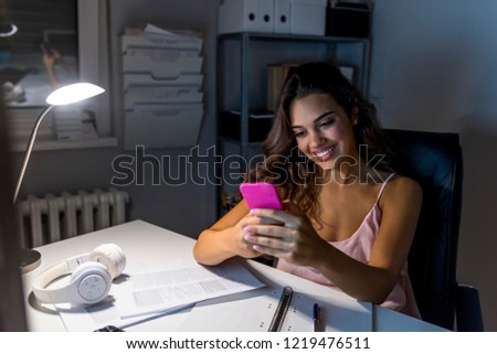 Smiling young female entrepreneur working from home, sending text messages on a cellphone. Happy woman using her phone working from home. Typing business message. 