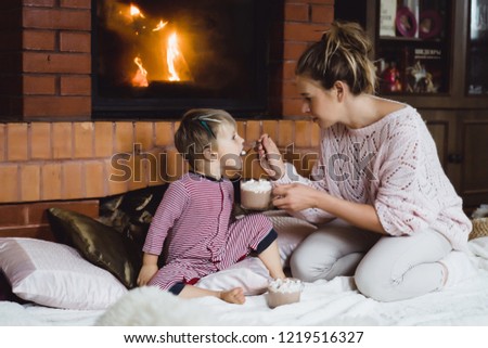 young woman with a child by the fireplace. mom and son drink cocoa with marshmello near the fireplace.
