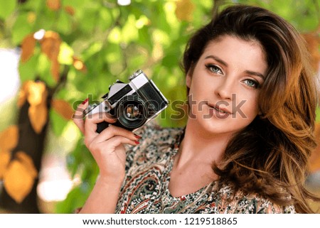 Beautiful and lovely woman holding a retro SLR camera and taking photos in an autumn park on a sunny day