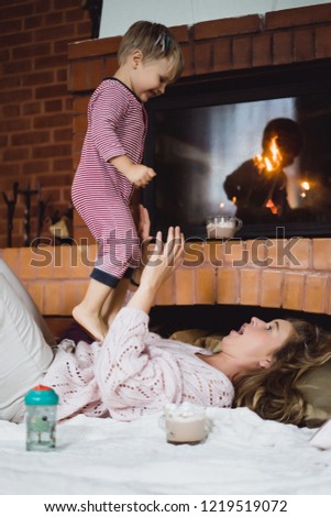 young woman with a child. Mom and son are fooling around, having fun near the fireplace.