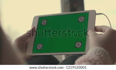 Hands of a girl holding a tablet with a green background