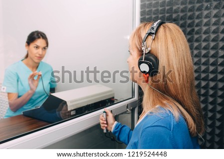 audiologist doing hearing exam to a mature patient using audiometer in special audio room.