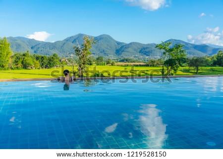 Women relax in the pool with mountain views and paddy fields.
