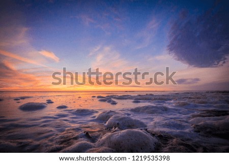 Amazingly colourful sea beach sunset with reflective orange and blue sand, foamy water and clouds on the Dutch Island Texel, Holland Europe