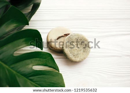 Zero waste concept. Natural eco friendly solid shampoo bar, green conditioner, soap on white wood with green monstera leaves. Eco products plastic free. Hair care and treatment