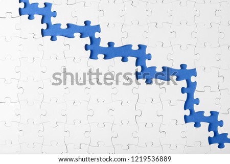 The assembled whole picture of white puzzles divided in half on a blue background with place for text. Symbol of teamwork and separation of duties.