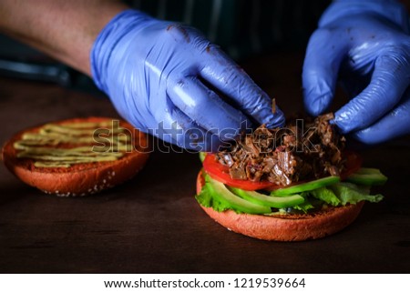 process of making burger. chef hands in gloves cooking beefburger with avocado and tomato