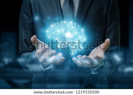A brain image consisted of different connections with the chip inside is hanging between the businessman's hands at the dark background. The concept is the artificial intelligence and brainstorming.