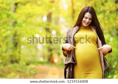  Happy pregnant woman pointing at her stomach in autumn colors park. Copy space                              