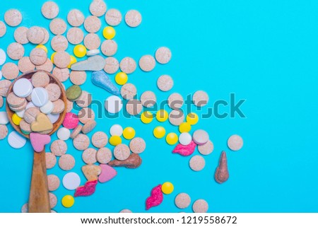 Assorted pharmaceutical medicine pills, tablets and capsules on wooden spoon on blue background. Copy space for text.