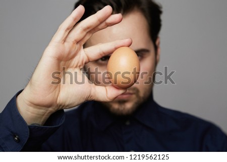 Confident man holding chicken fresh organic egg front of FACE ON GRAY BACKGROUND. Close up