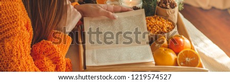 Soft cozy photo of woman in warm orange sweater on the bed with cup of tea and fruit. Girl sitting on the bed with old books. Reading a book, concepts of home and comfort, place for text