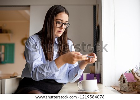 Woman with dark hair, glasses, blue shirt sitting in a cafe and taking pictures of your coffee