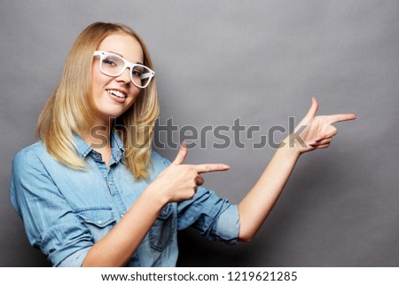 Portrait of cheerful young woman showing copyspace, visual imaginary or something, or pressing virual button,  over grey  background