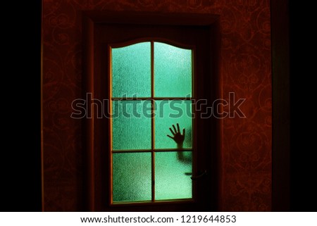 Dark silhouette of hand behind glass in supernatural green light. Locked alone in room behind door on Halloween. Nightmare of child with aliens, monsters and ghosts. Evil in home. Inside haunted house
