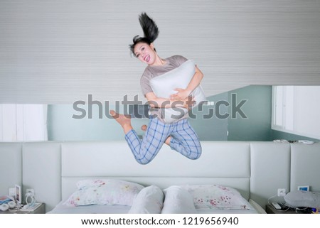 Picture of happy woman hugging a pillow while jumping on the bed. Shot at home