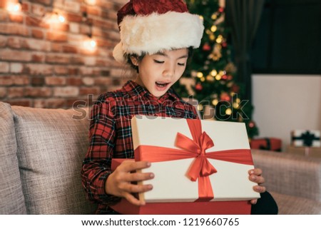 kid with red hat surprised by the magical shiny xmas gift box. little girl opening the present received from santa claus on boxing day. childhood on christmas eve at night at home concept