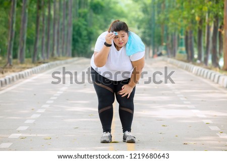 Picture of fat woman looks tired after jogging on the road while wiping her sweat