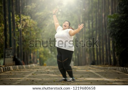 Picture of fat woman wearing sportswear while lifting hands to celebrating her success on the road