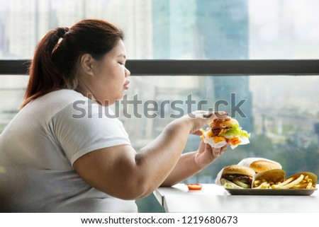 Picture of overweight woman eating hamburgers in the restaurant while sitting by the window