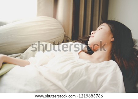 Image of a woman sleeping on a bed, wearing white shirt.
