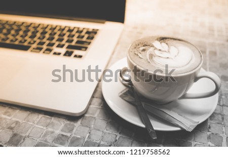 A cup of capuchino coffee or latte coffe in a white cup with laptop on table. Royalty high quality free stock photo of drink capuchino or latte coffe with laptop for working in office
