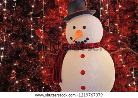 Large snowman in front of sparkling artificial red pine trees for Christmas indoor decoration
