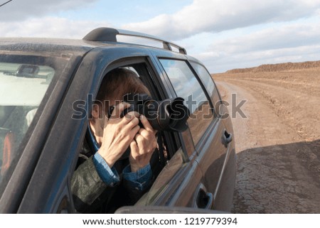 Photographer man taking pictures of the landscape from the car window. Around agricultural fields and wheat.
