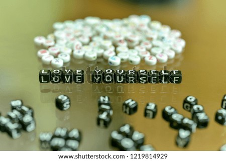 LOVE  YOURSELF  written with Acrylic Black cube with white Alphabet Beads on the Glass Background