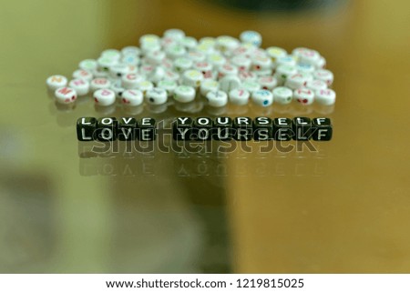LOVE YOURSELF  written with Acrylic Black cube with white Alphabet Beads on the Glass Background