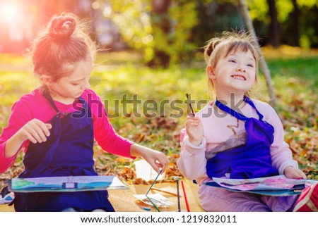 Two little sisters drawing together in fall park. Creative funny child painting on nature sitting on the ground. Outdoors activity for school age children concept.