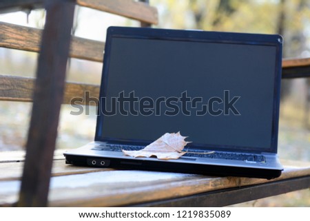 Opened laptop lies on a bench in autumn park