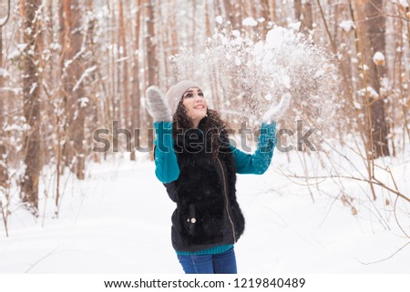Season, leisure and people concept - young woman is happy and throwing snow in the winter nature