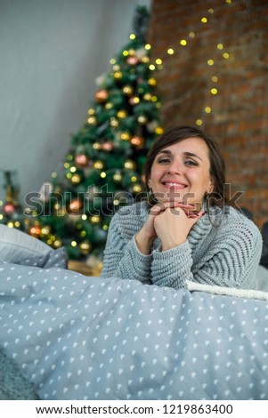 Young Women is lying and smiling on the Bed near the Cristmas Tree