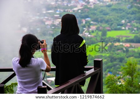 Women are standing facing the view and another woman is taking a photo. On the balcony It has a natural background and fog. Phu Bo Bit, Loei, Thailand. 