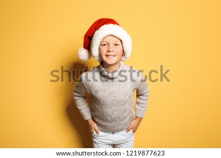 Cute little boy in warm sweater and Christmas hat on color background