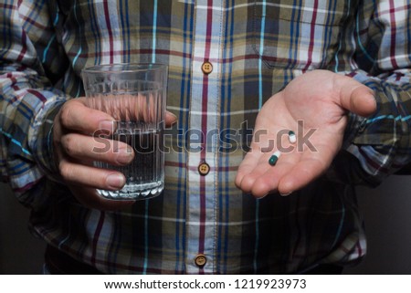 Cropped image of a sick person holding a tablet and a glass of water, on a gray background, hands of a working man.
