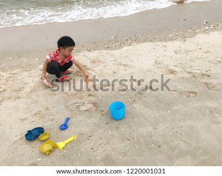 A happy Asian boy in red shirt is playing toy and sand  on the beach in holiday.