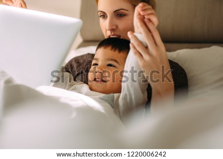 Little boy with mother enjoying watching cartoon movie on laptop while lying in bed. Young woman with her son looking at laptop with her hands raised.