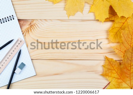 An open notebook and a ruler with two pencils on a wooden background and autumn leaves. School supplies, learning, planning. There is some free space for your text or sign.