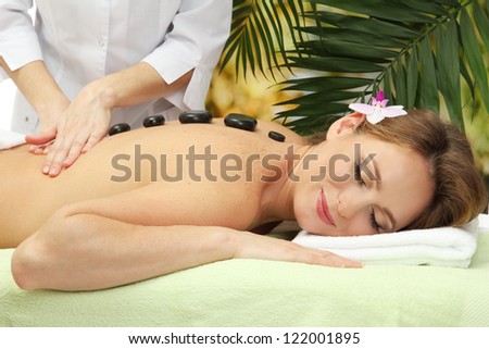 beautiful woman in spa salon  getting massage with stones, on palm leaves background