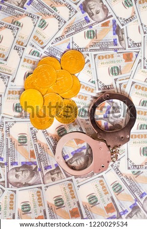 Police handcuffs and bitcoins lie on a large number of dollar bills. The concept of problems with the law during the illegal cryptocurrency mining and bitcoin operations.