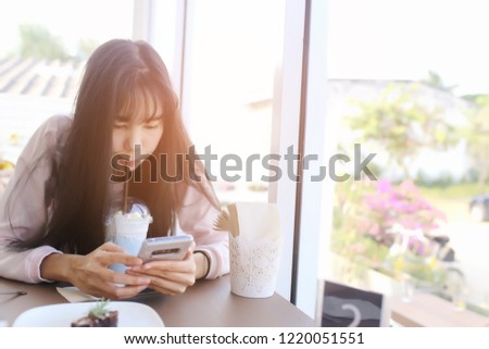 Beautiful chic cute Asian woman look down on smart phone in hand at coffee shop with blue color milk ice unicorn beverage plastic glass on wood table in alone valentine day.