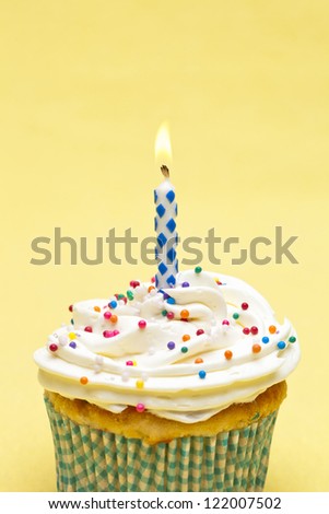 Image of a cupcake with candle isolated on yellow background.