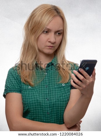 angry young woman in casual green shirt with smartphone in hand looking at phone